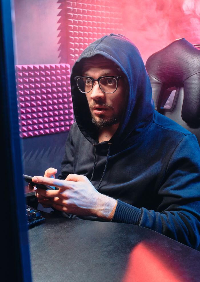 Man in black hoodie working on smartphone in dim cyber environment.